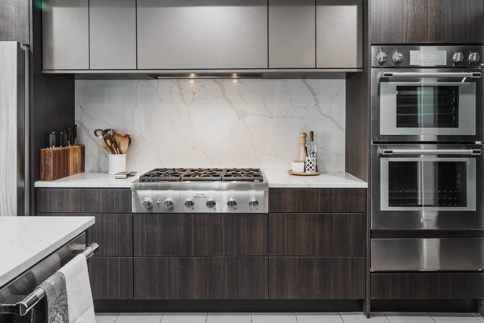 Feature wall with built-in wall ovens, quartz backsplash, and sleek cooktop 